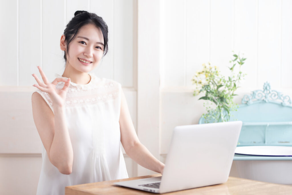 パソコンの前でOKサインを作る女性